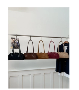 Detail view of five suede shoulder bags in different colors hanging on a metal display rack