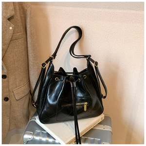 Detail of black quilted leather bucket bag with drawstring and vintage hardware on a suitcase