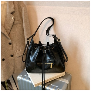 Detail of black quilted bucket bag with drawstring closure and golden metal hardware