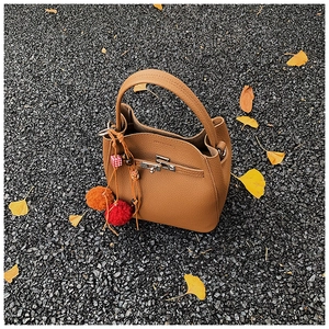 Close-up of brown litchi pattern leather bucket bag with colorful tassel on autumn street