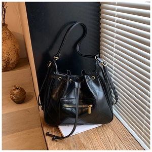 Detail of black quilted bucket bag with golden zipper and leather drawstring closure