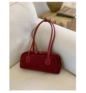 Detail of dark red suede Boston bag with double zippers and stitching on a sofa