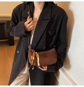 Close-up of brown suede shoulder bag with decorative wooden and white beaded tassel