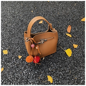 Detail of caramel bucket bag with lychee texture and colorful pompom on autumn leaves