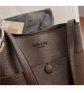 Detail of dark brown leather tote with embossed logo and metal circular buckle