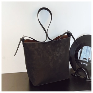 Detail view of large black matte suede bucket bag with contrast brown lining on a dark surface