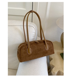 Close-up of brown suede Boston bag with white contrast stitching on a white sofa