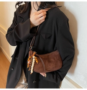 Detail of a brown suede half-moon bag featuring a multi-color beaded tassel and leather strap