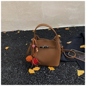 Brown bucket bag with litchi texture and colorful ethnic tassel on dark gravel ground