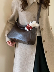 Deep brown leather crossbody bag with cute puppy pendant on beige coat model