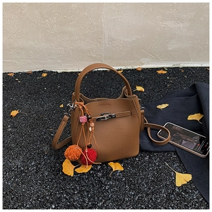 Detail view of brown pebbled leather bucket bag with metallic buckle and colorful pom-poms