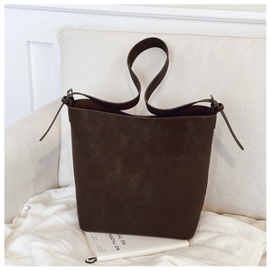 Detailed close-up of dark brown suede bucket bag with adjustable strap and metal hardware
