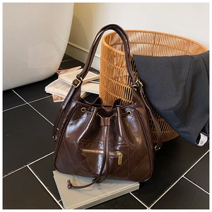 Detailed view of dark brown quilted drawstring bucket bag with metallic zipper on vintage books