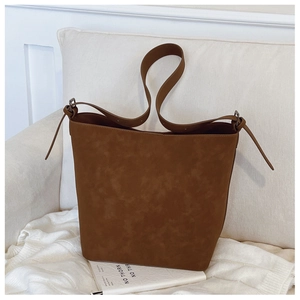 Close-up of brown suede bucket bag with adjustable strap on a white sofa and cozy throw