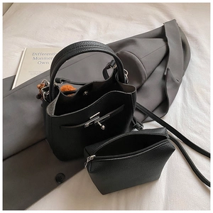 Detail of black lychee grain leather bucket bag set with inner pouch and orange pom-pom