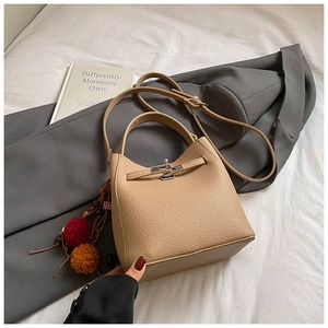 Detail of beige lychee leather bucket bag with metal twist lock and colorful pompom
