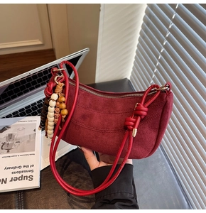 Detail of burgundy suede dumpling bag featuring knot handles and decorative wood beads