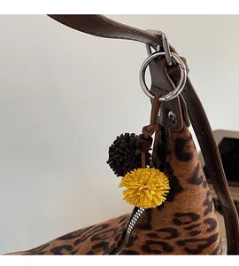 Detail of leopard print tote bag featuring a decorative pompom charm and leather strap