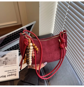 Detail of burgundy suede crescent bag with smooth leather strap and wooden bead charm