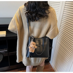 Detail of black matte PU leather shoulder bag with a cute brown plush bear charm accessory