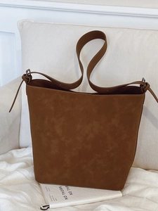 Vintage brown faux suede bucket bag with adjustable strap on a minimalist sofa