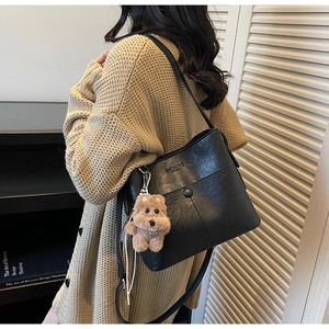 Detail of vintage black faux leather tote bag with plush puppy charm on a model
