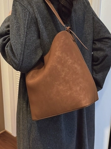 Brown leather bucket bag with large capacity worn by a model in a charcoal grey wool coat