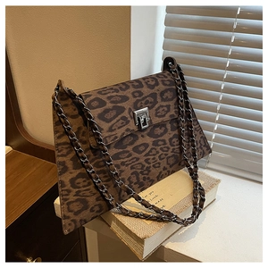 Detail of leopard print handbag with metal clasp and chain strap on decorative books