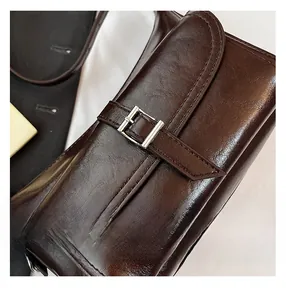 Detailed close-up of polished brown leather texture and silver buckle on a stylish pillow bag