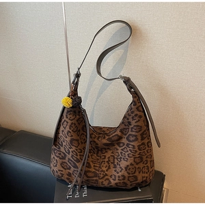Detail of leopard print tote bag featuring a plush pom-pom charm and adjustable strap