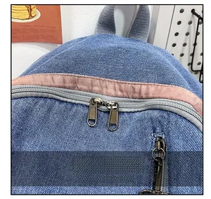 Close-up of smooth metal zippers and pink fabric trim on blue denim backpack top
