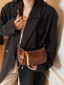 Brown suede crescent bag with wooden bead charm worn by a model in a black blazer