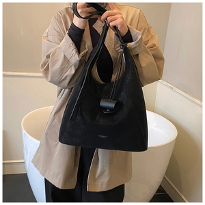Gros plan d'un sac cabas en daim noir avec bandoulière large et logo de la marque