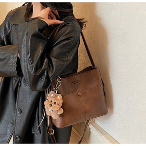 Detail of dark brown leather bag with fashion text and cute teddy bear plush charm