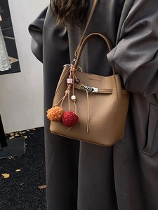 Brown lychee leather bucket bag with metal lock and colorful fur ball charms on a model