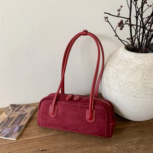 Detail of burgundy suede baguette bag featuring white contrast stitching and long handles