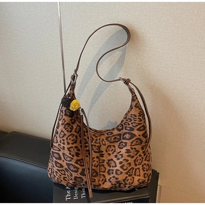 Detailed view of leopard print hobo bag with yellow pom-pom and pinecone charm on a book