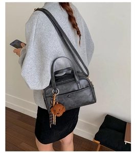 Détail d'un sac bowling noir en similicuir avec charm ours en peluche et pompon chic