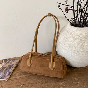 Close-up of vintage brown suede baguette bag with smooth leather strap and dual zippers