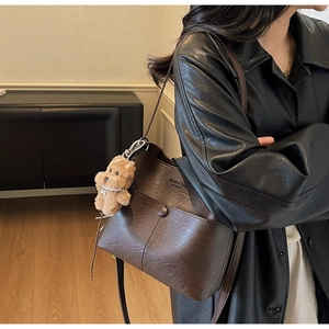 Detail of dark brown PU leather bucket bag featuring a decorative pocket and plush bear charm