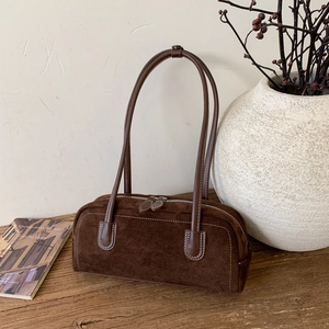 Detail of vintage dark brown suede baguette bag with contrast stitching on wooden surface