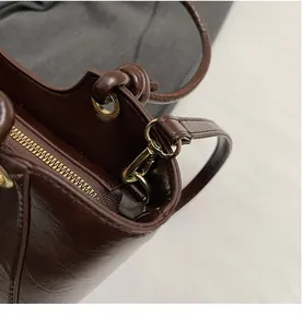 Détail du sac seau en cuir ciré marron avec crochets dorés et poignée à nœuds élégante