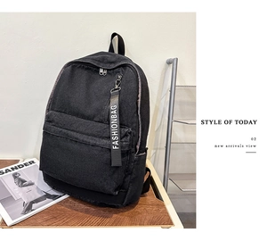 Detail of black denim backpack with 'FASHIONBAG' ribbon on a rustic wooden desk