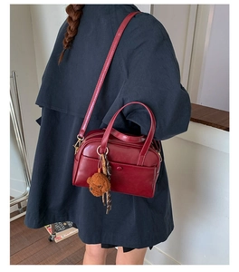 Detailed view of burgundy leather boston bag with a cute plush bear charm on the strap