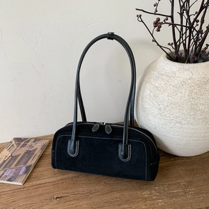 Detailed view of black suede baguette bag with contrast white stitching on a wooden surface