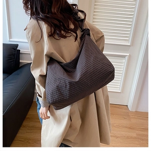 Detail of wide pleated shoulder strap on large checkered canvas dumpling bag