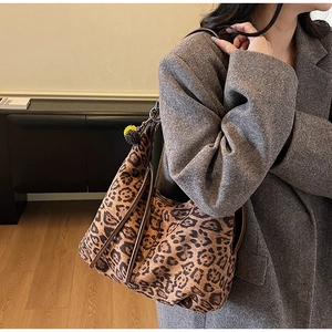 Detailed side view of a large leopard print hobo bag with brown shoulder strap and pompom