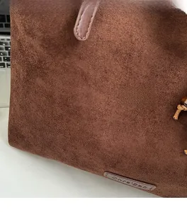 Détail de la texture douce du cabas en daim marron et étiquette en cuir sur le côté