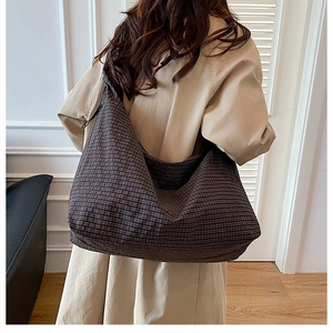 Detail of a large dark checkered canvas hobo bag worn by a model in a beige coat