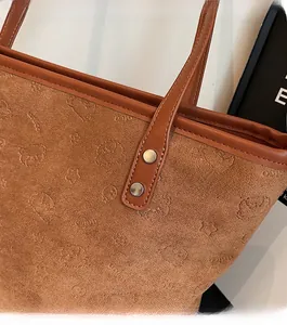 Detail of reinforced silver rivets and vintage embossed bear pattern on brown tote bag